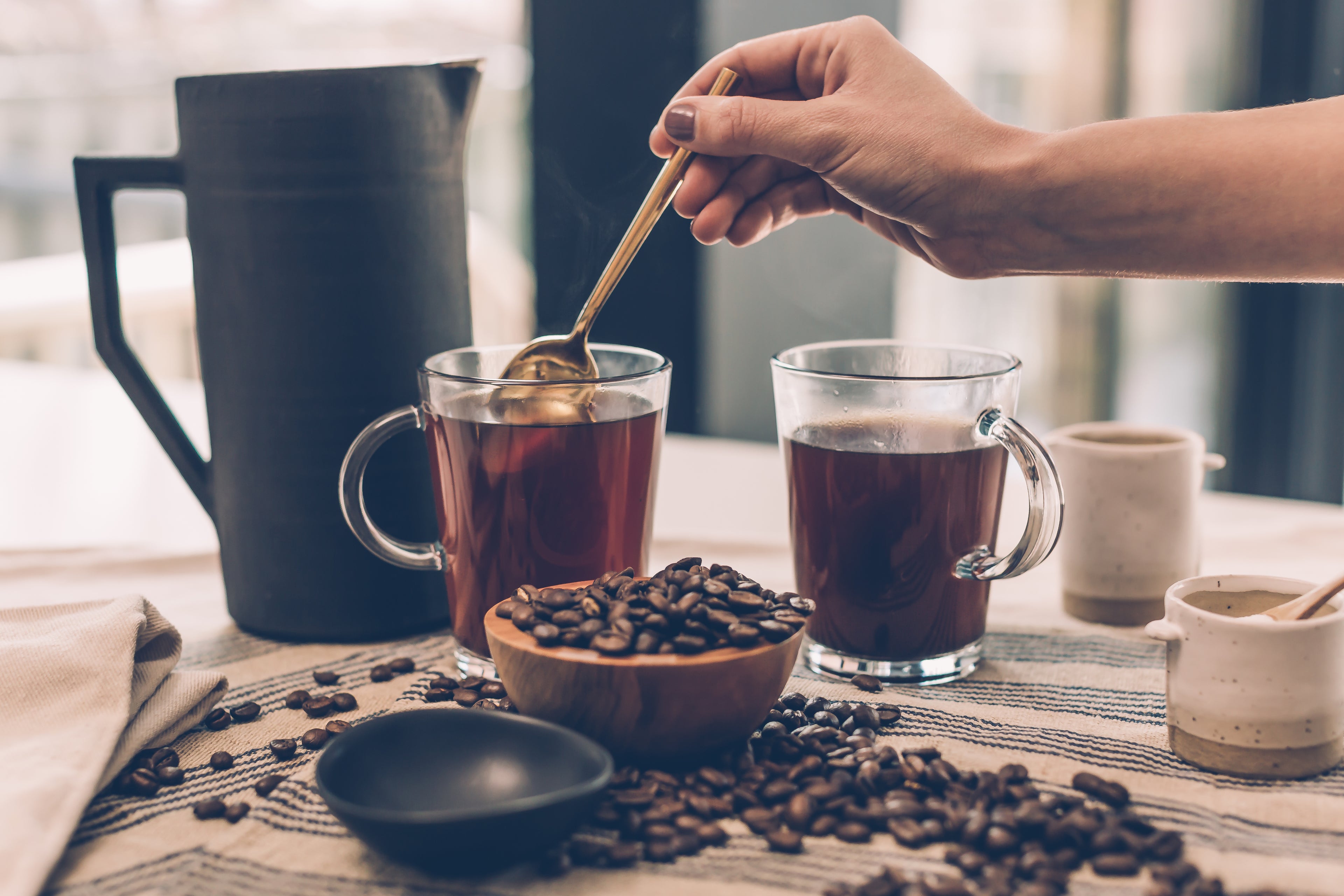 two full coffee cups with someone stirring one of them