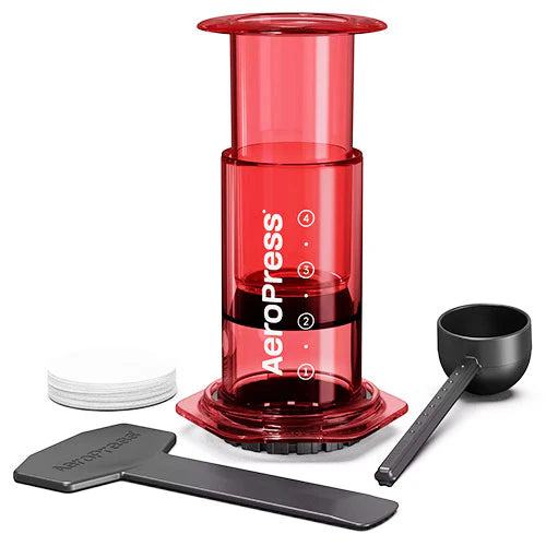 Red AeroPress coffee maker with black scoop and white components on a white background