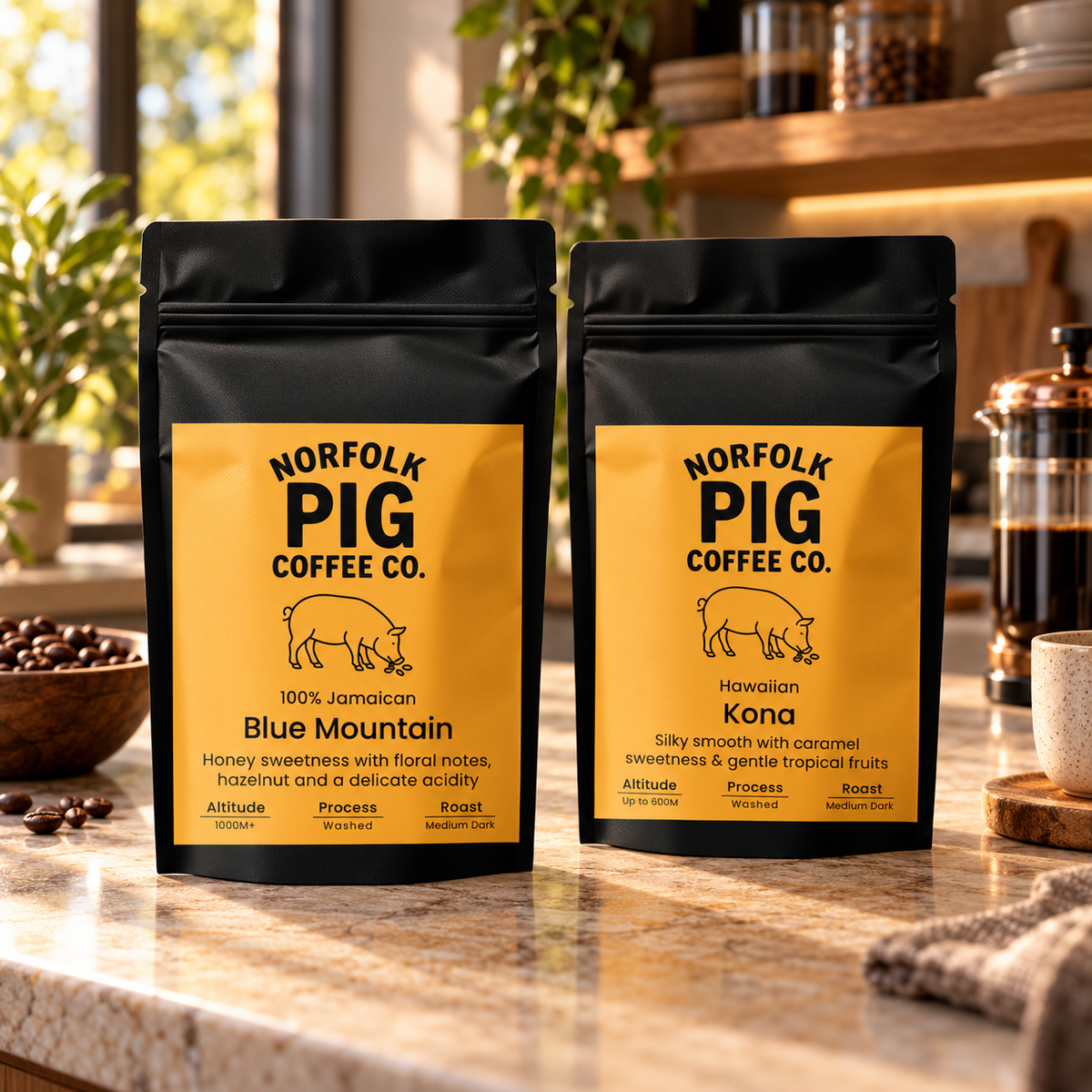 Two stand-up coffee pouches from Norfolk Pig Coffee Co. on a kitchen counter, one labeled Blue Mountain and one labeled Kona, with coffee beans and a French press in a warm kitchen setting.