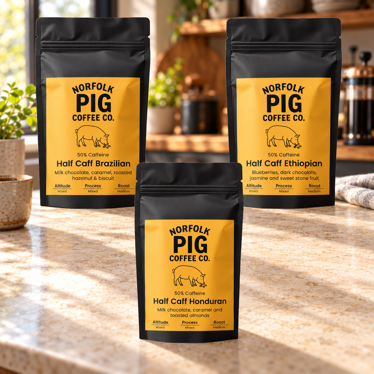 Three black stand-up coffee pouches from Norfolk Pig Coffee Co. are arranged on a kitchen countertop.