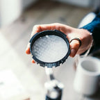 Person holding a coffee filter with water droplets over a blurred kitchen background