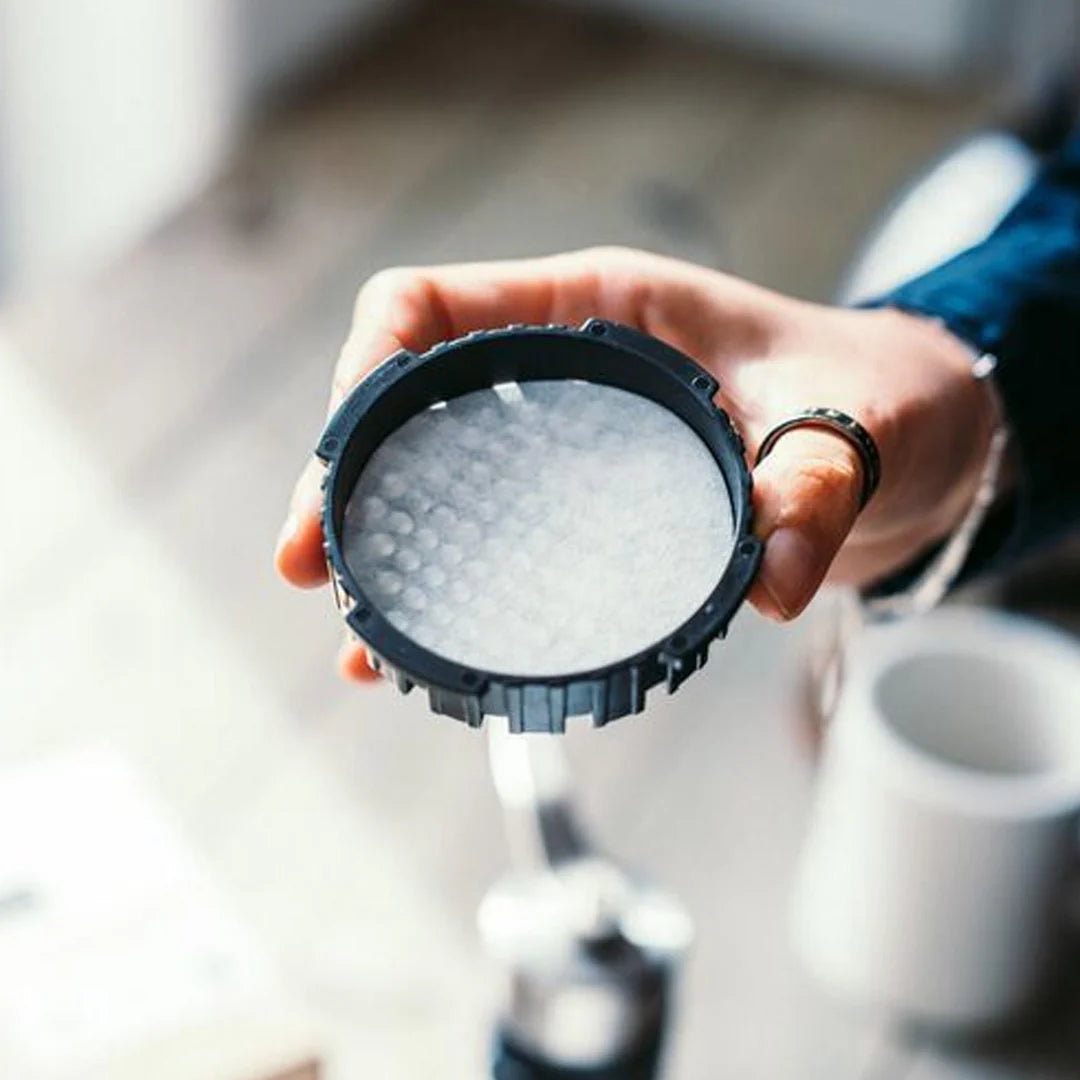 Person holding a coffee filter with water droplets over a blurred kitchen background