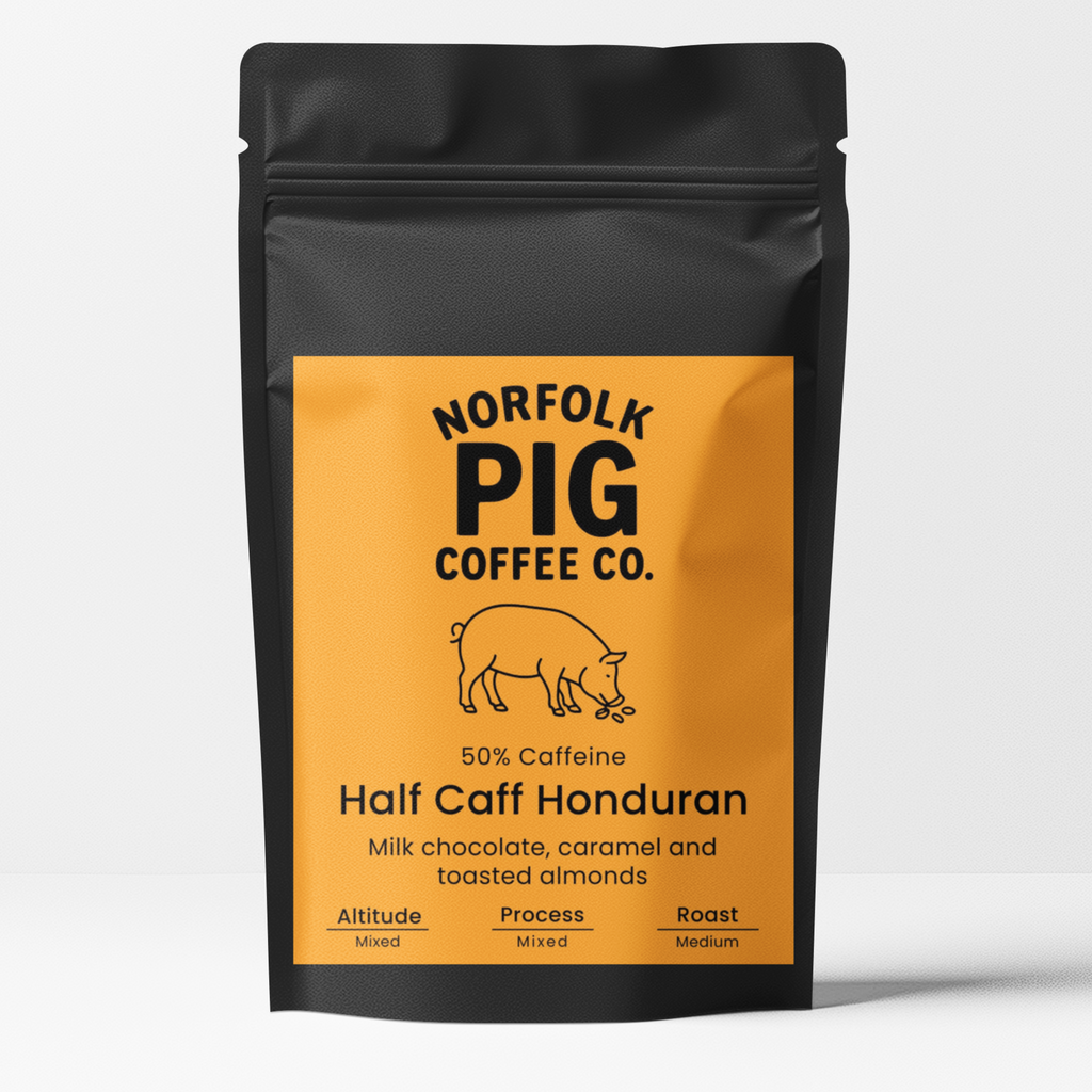 A black stand-up pouch of Norfolk Pig Coffee Co. Half Caff Ethiopian coffee with a bright orange label, shown on a light gray background.