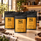 Three bags of Norfolk Pig Coffee Co. coffee stand on a kitchen counter with coffee beans and a French press in a warm, sunlit kitchen setting.