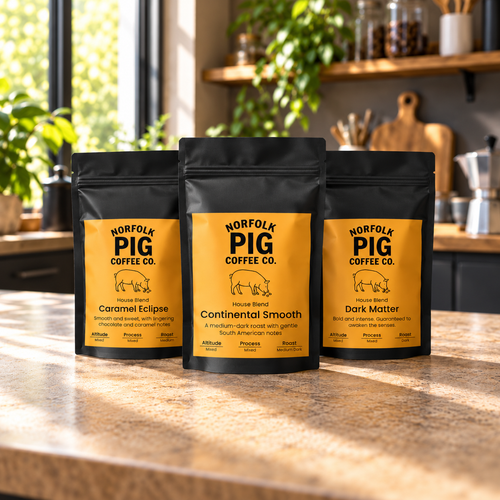 Three black coffee bags from Norfolk Pig Coffee Co. stand on a kitchen counter, with a warm yellow label on each package.