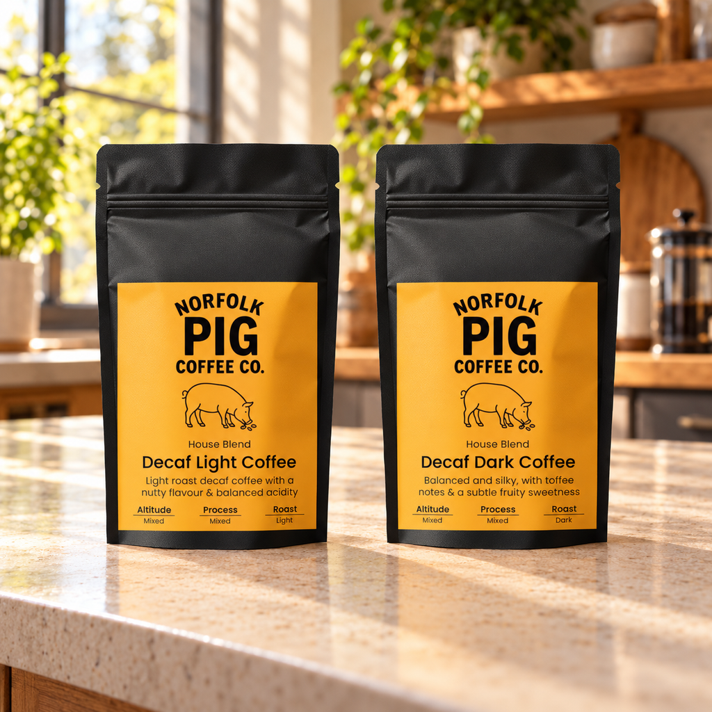 Two black stand-up coffee bags labeled Norfolk Pig Coffee Co. Decaf Light and Decaf Dark, standing on a kitchen counter with a blurred kitchen background.