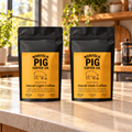 Two black stand-up coffee bags labeled Norfolk Pig Coffee Co. Decaf Light and Decaf Dark, standing on a kitchen counter with a blurred kitchen background.